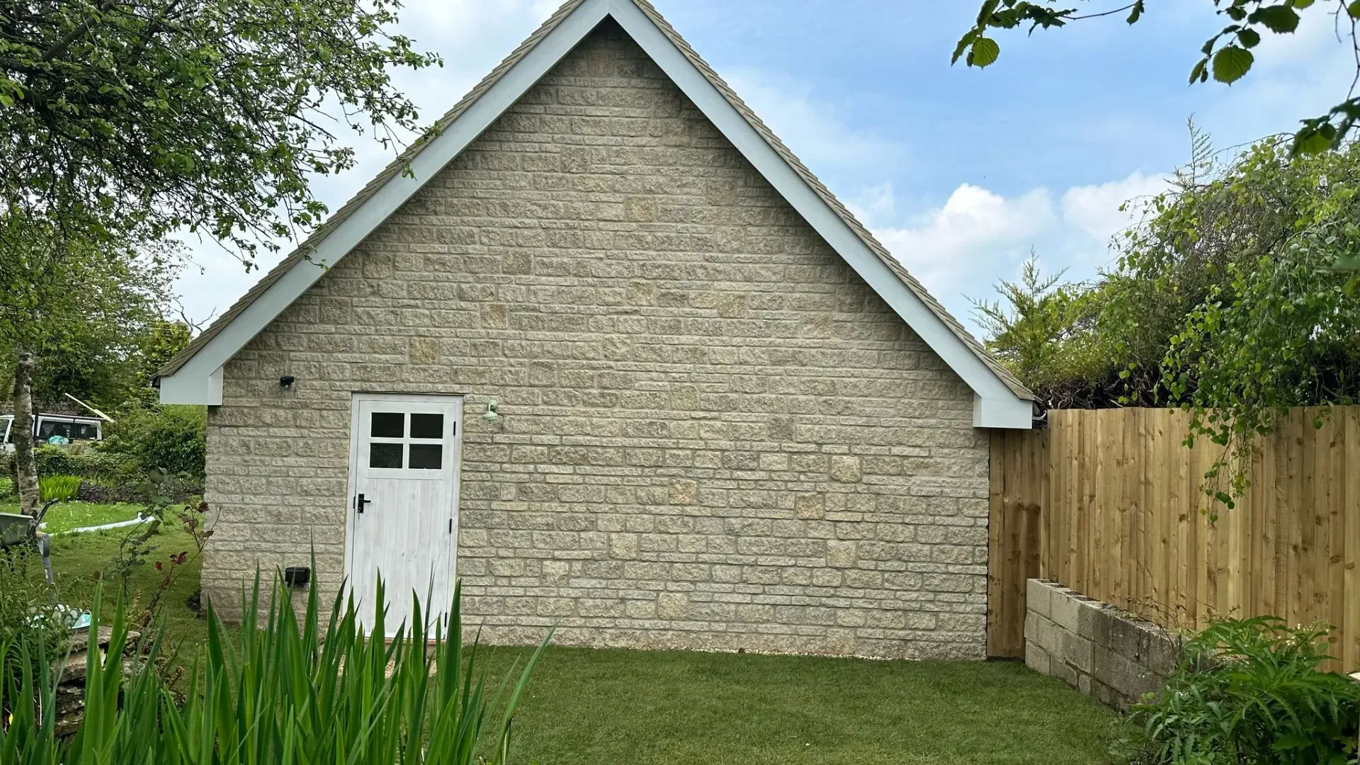 Completed stone building extension with white door and neat garden by DP Carpentry & Building LTD, Gloucestershire builders.